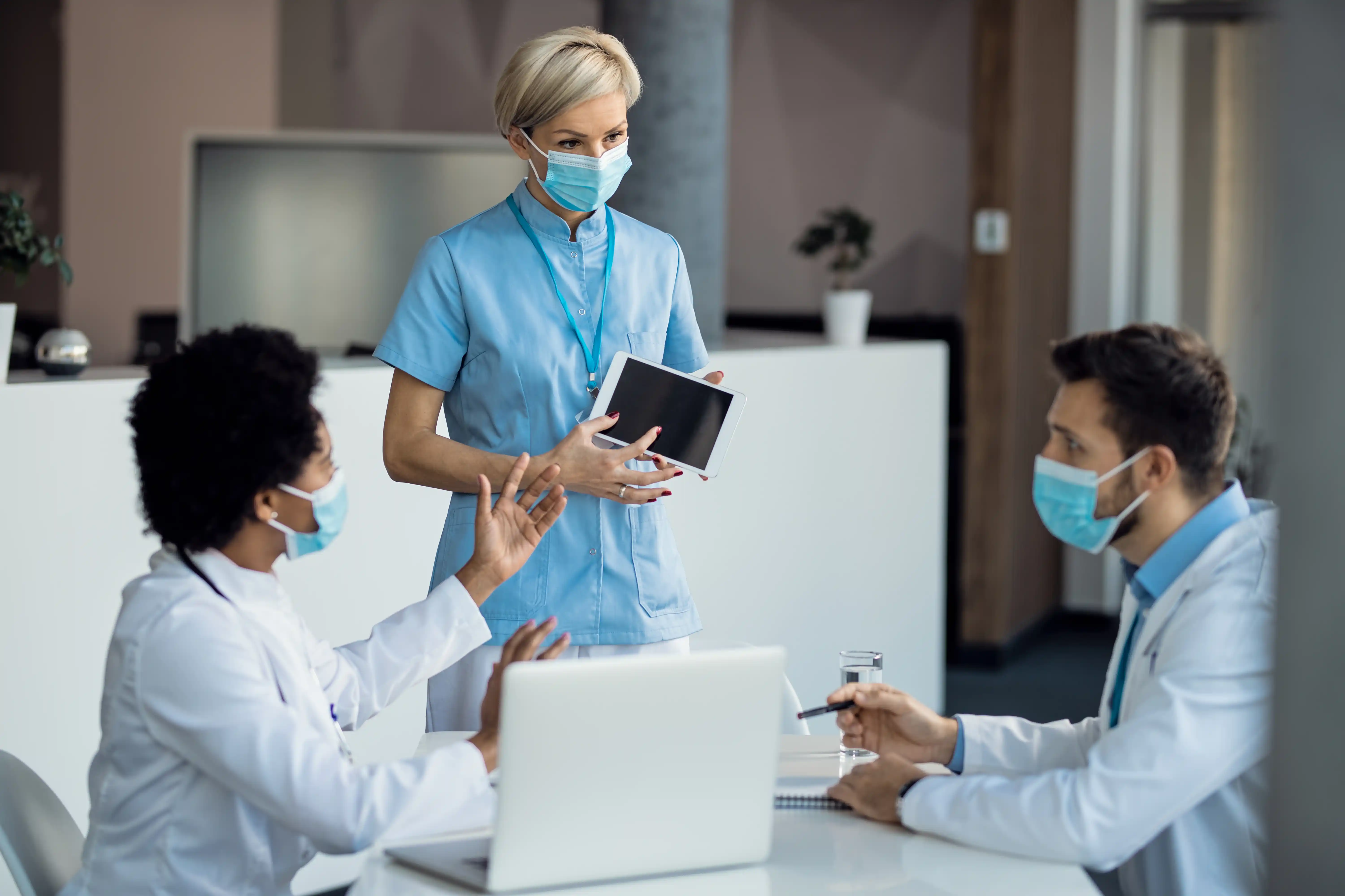 A woman in a medical mask converses with three doctors in a clinical setting.