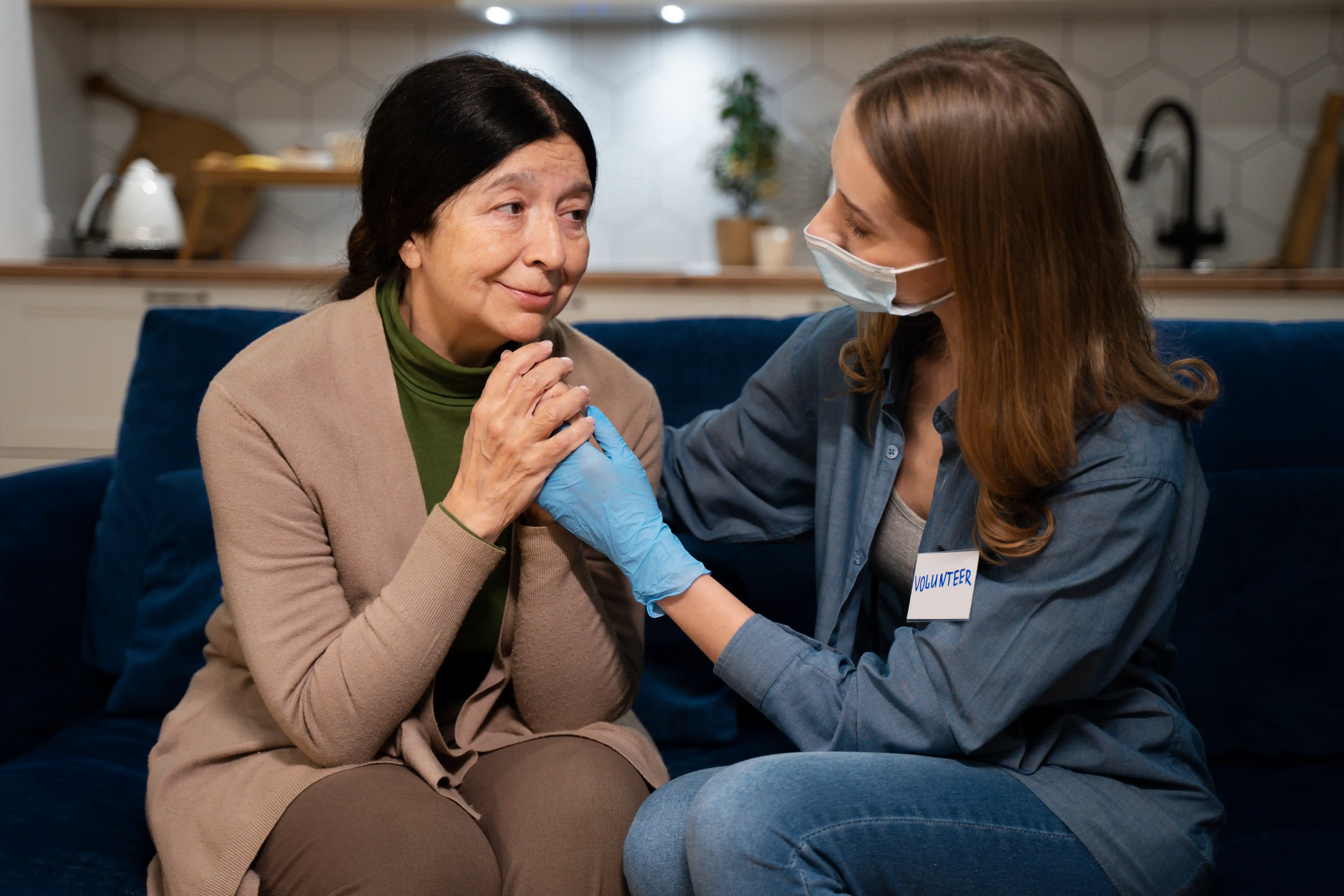 A woman is seated on a couch with a nurse, discussing medical care and support in a comfortable setting.