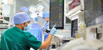 Lets-collaborate A medical team in blue scrubs conducts surgery in an operating room. A technician in green monitors vital signs on a screen, ensuring patient safety.